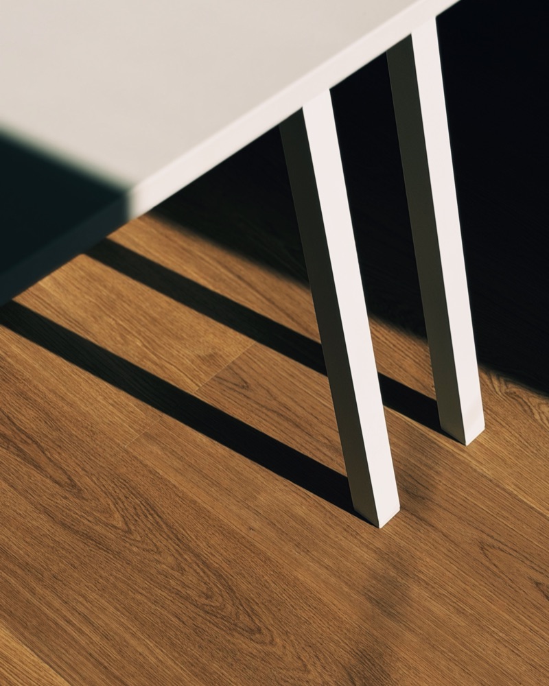 Les pieds blancs d'un bureau de la Bibi House sur le parquet en chêne, au soleil.