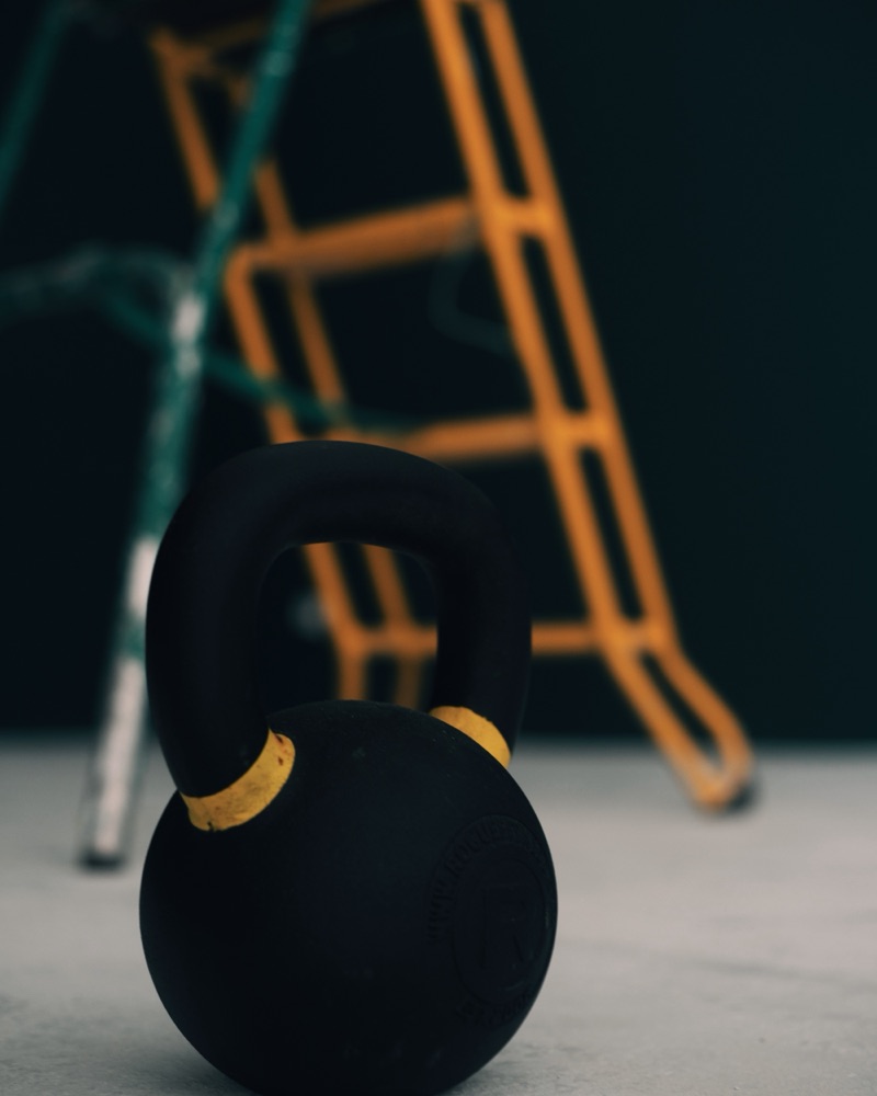 Une kettlebell sur le sol de La Salle, la salle de sport du coworking Bibi House à Biarritz, devant le mur vert sombre.
